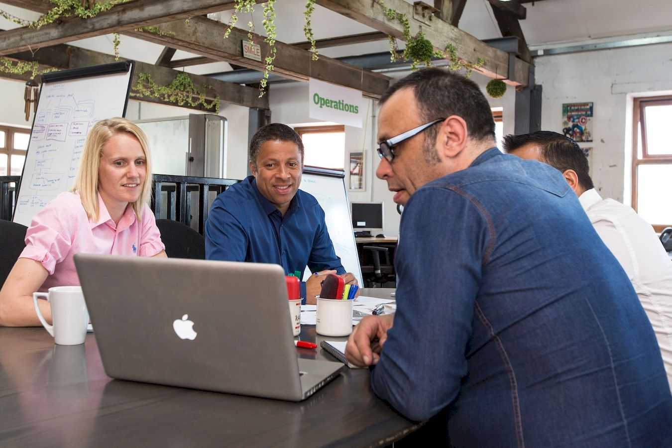four adults having a work meeting and looking at a laptop